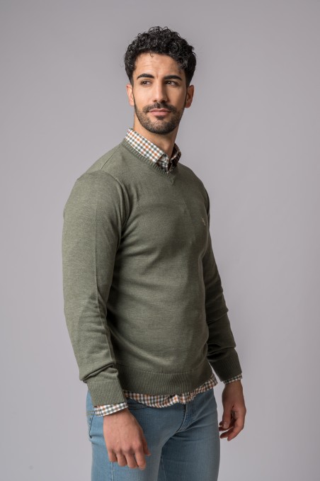 Homem com camisola verde e camisa xadrez sobre fundo cinzento