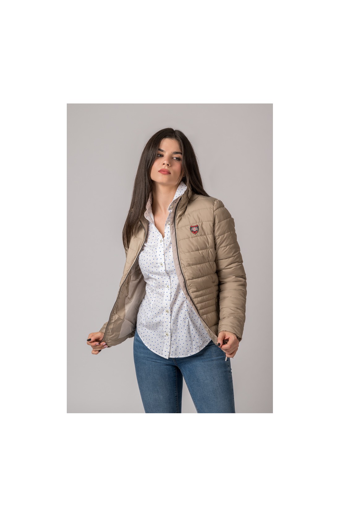 Mulher com casaco bege acolchoado e camisa branca de pontos azuis