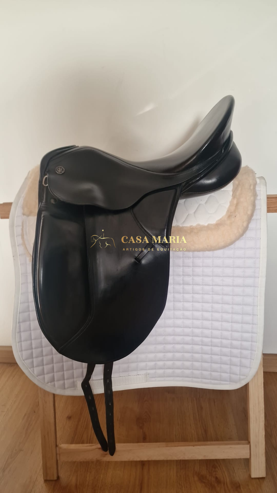 Sela de equitação de couro preto sobre cavalo branco acolchoado em suporte de madeira
