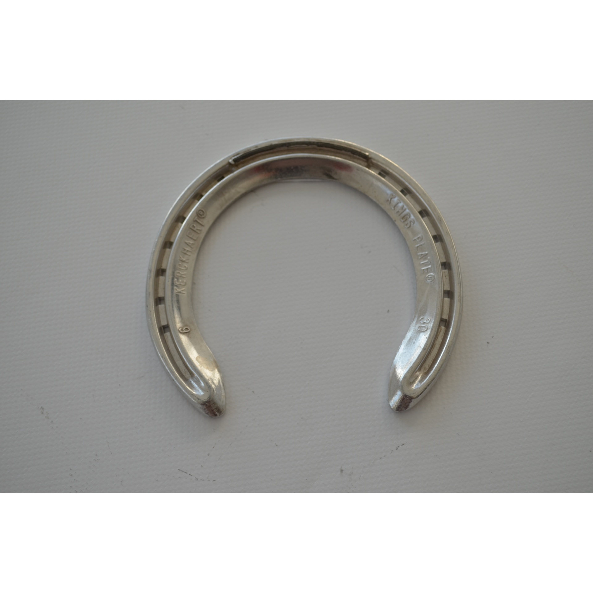 Ferradura metálica prateada com gravações em fundo branco