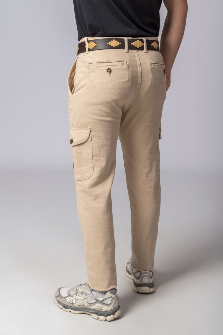 Calças bege com bolsos e cinto castanho com padrões, usadas com sapatilhas cinza e camiseta preta.