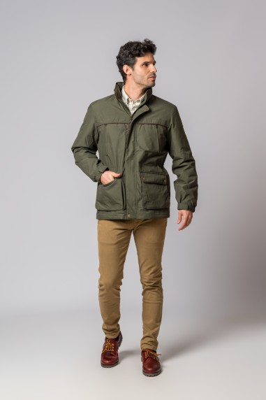 Homem a usar casaco verde, camisa branca, calças castanhas e sapatos castanhos.