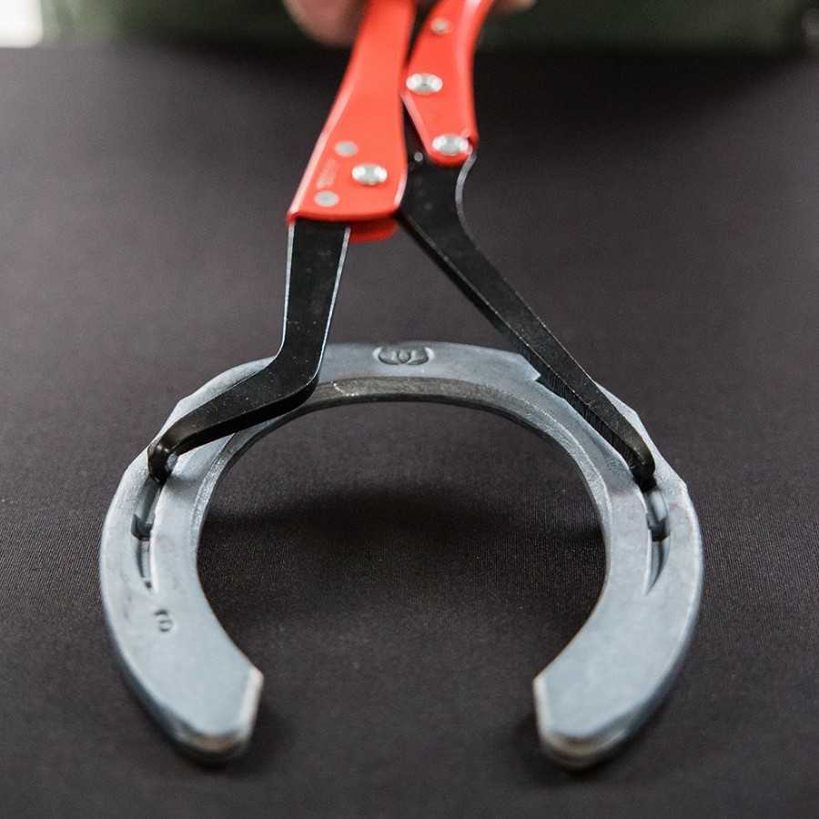 Alicate com cabo vermelho segurando uma ferradura cinzenta de metal