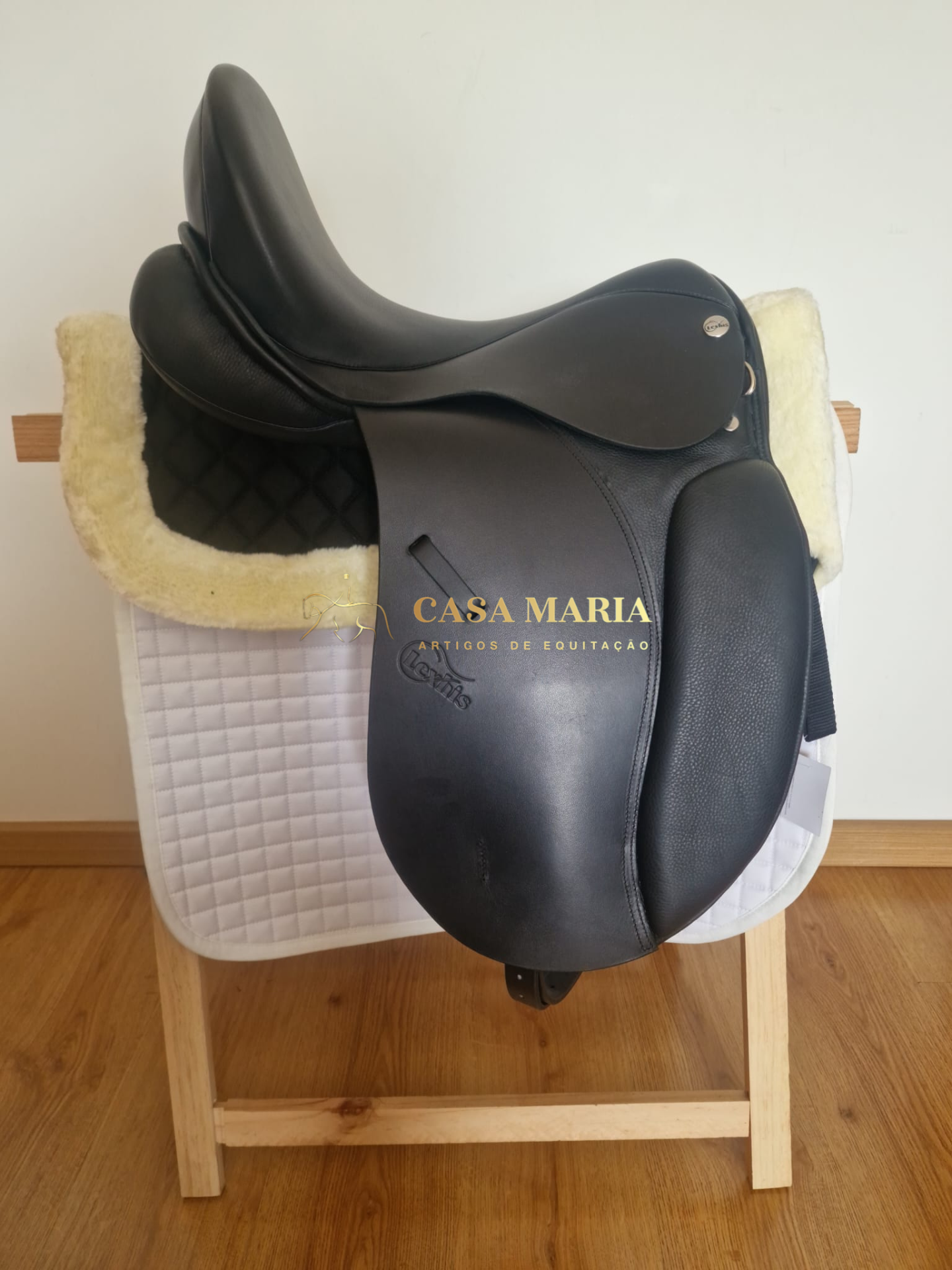 Sela de equitação preta sobre mantas branca e preta num suporte de madeira