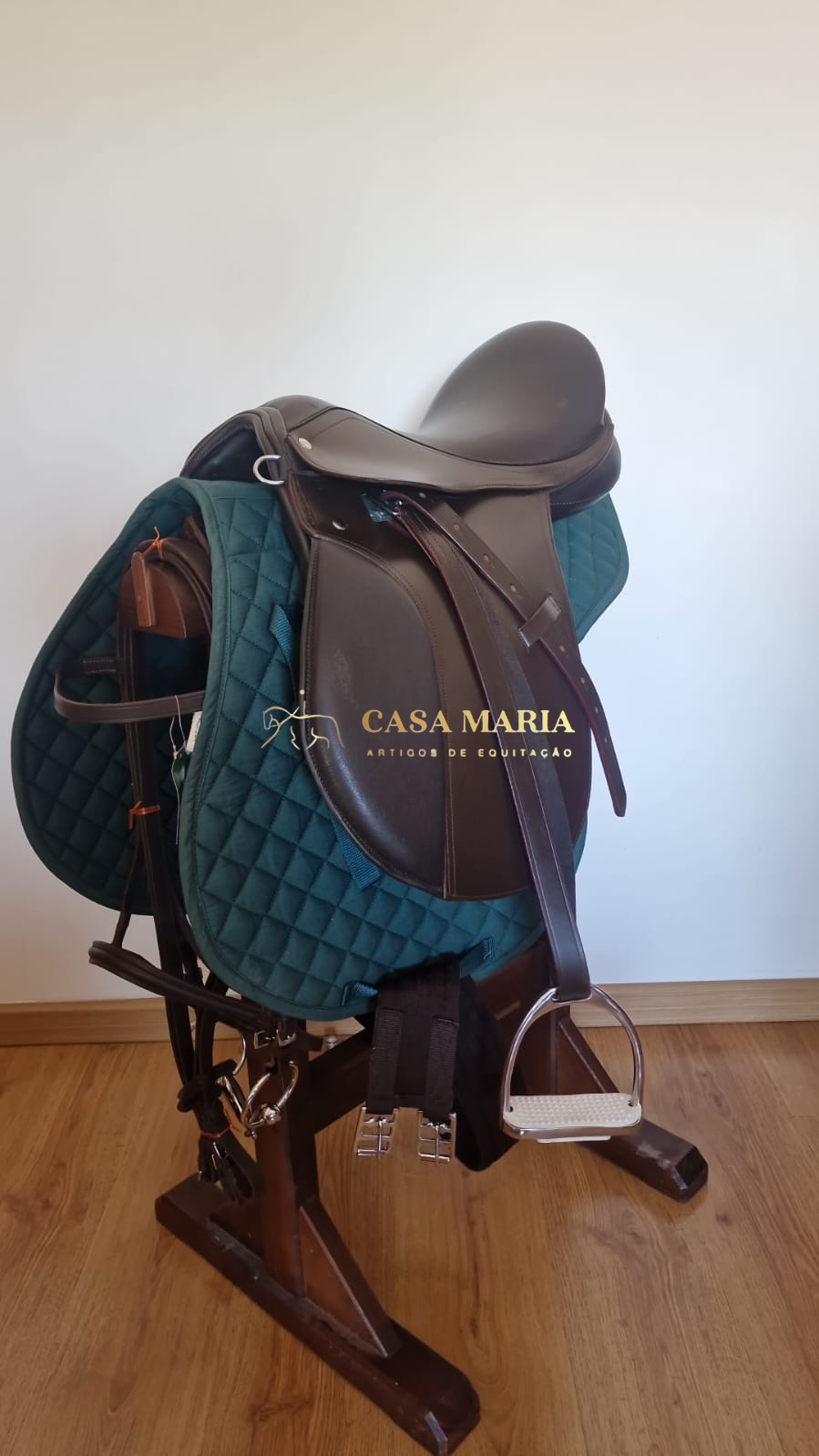 Sela de equitação castanha com almofada verde em suporte de madeira