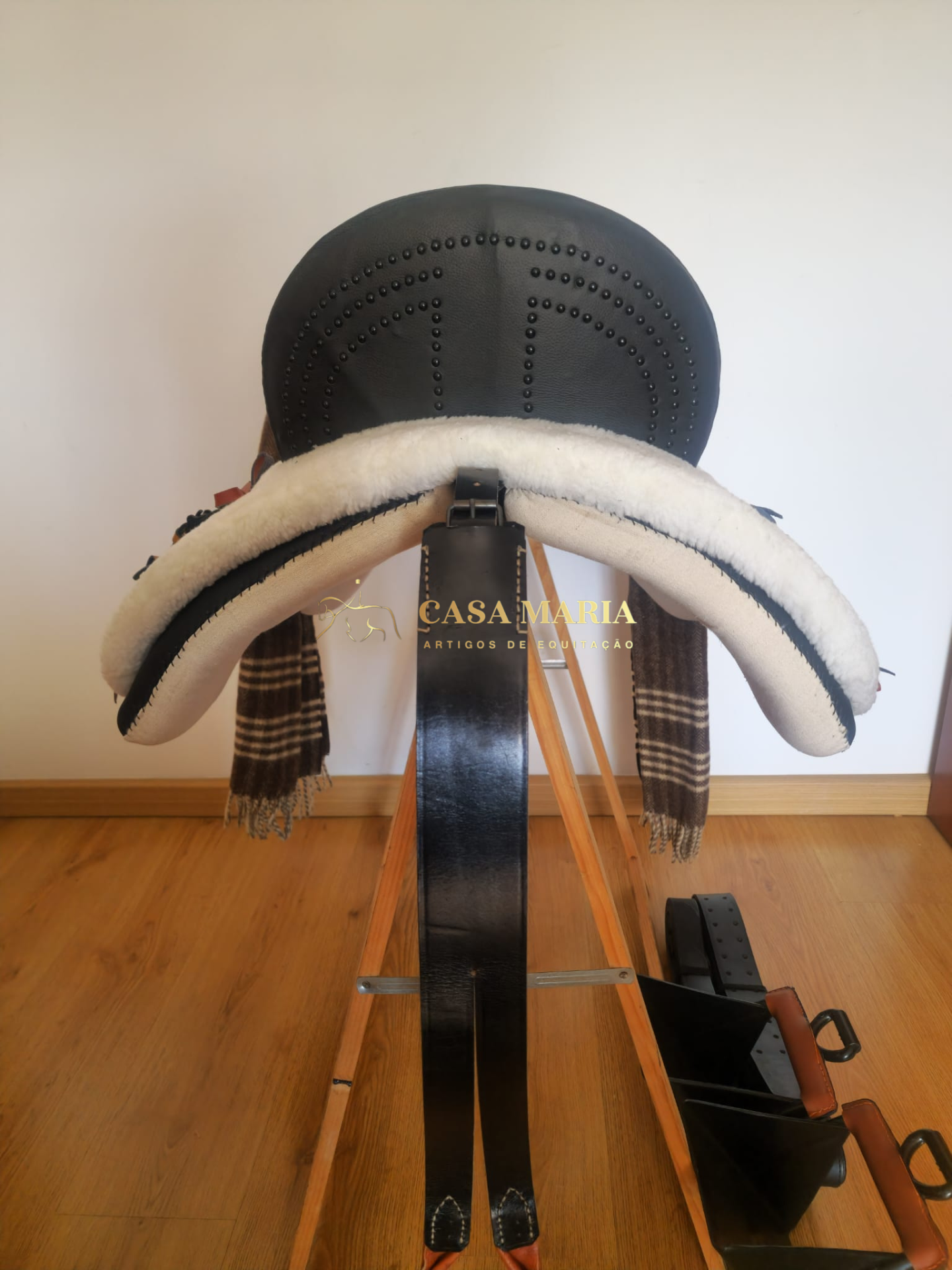 Sela preta de couro com tachas e forro branco em suporte de madeira