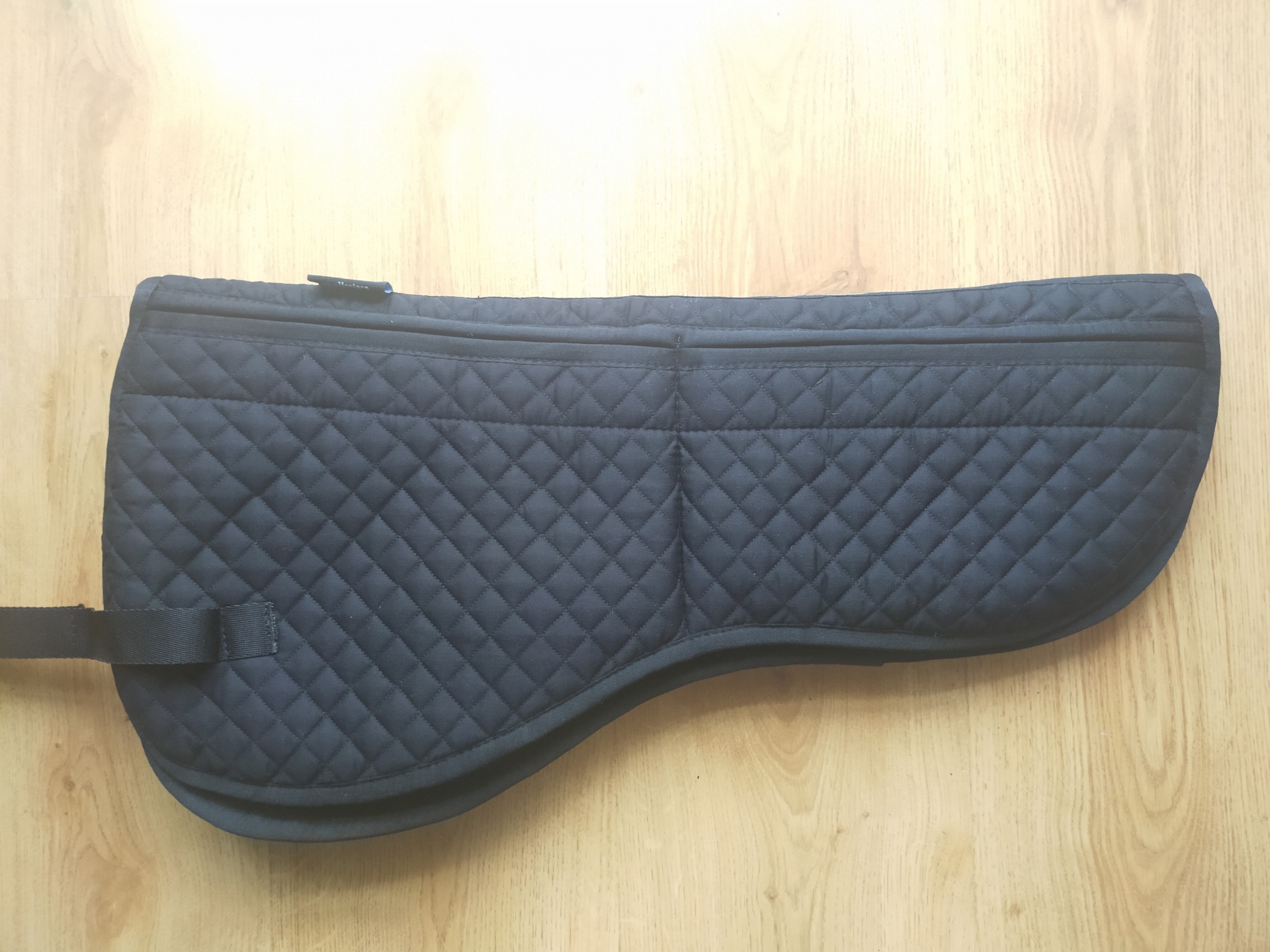 Protetor de sela de cavalo preto acolchoado com tira de velcro sobre piso de madeira