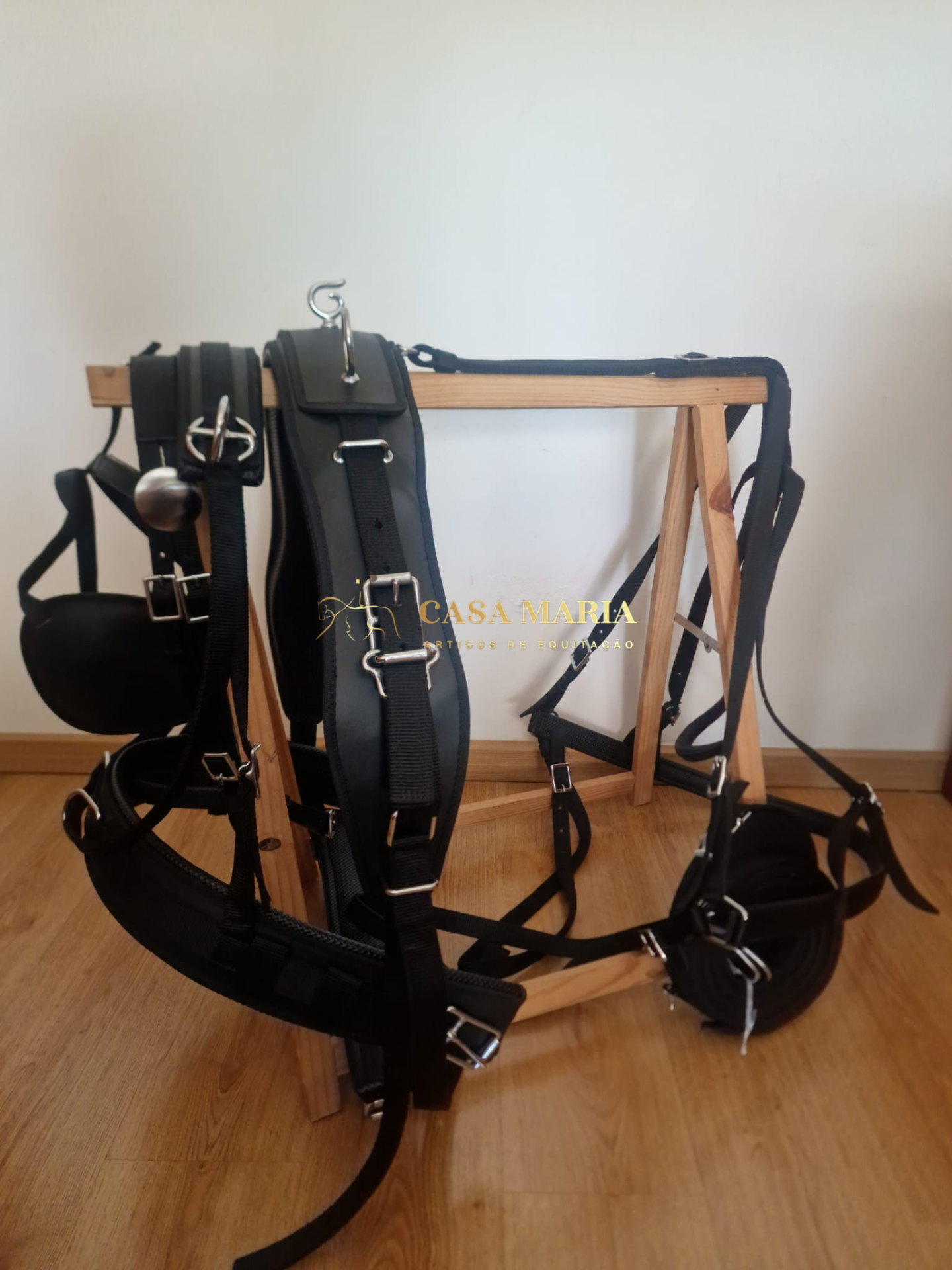 Arnês preto com fivelas metálicas num suporte de madeira