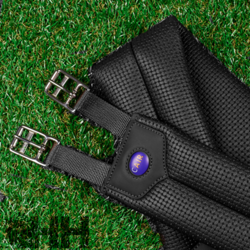 Cinchas pretas para cavalo com fivelas metálicas e brasão azul 'CAMP' sobre relva verde