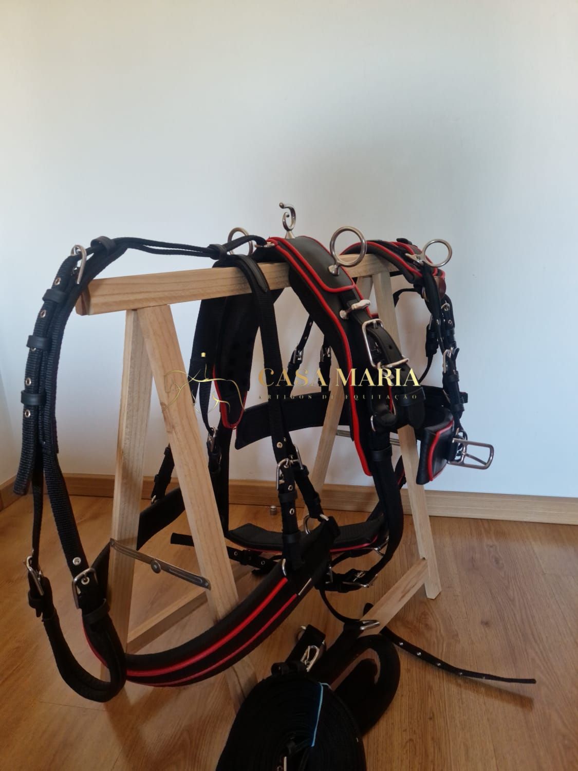 Conjunto de arreio preto e vermelho pendurado num suporte de madeira