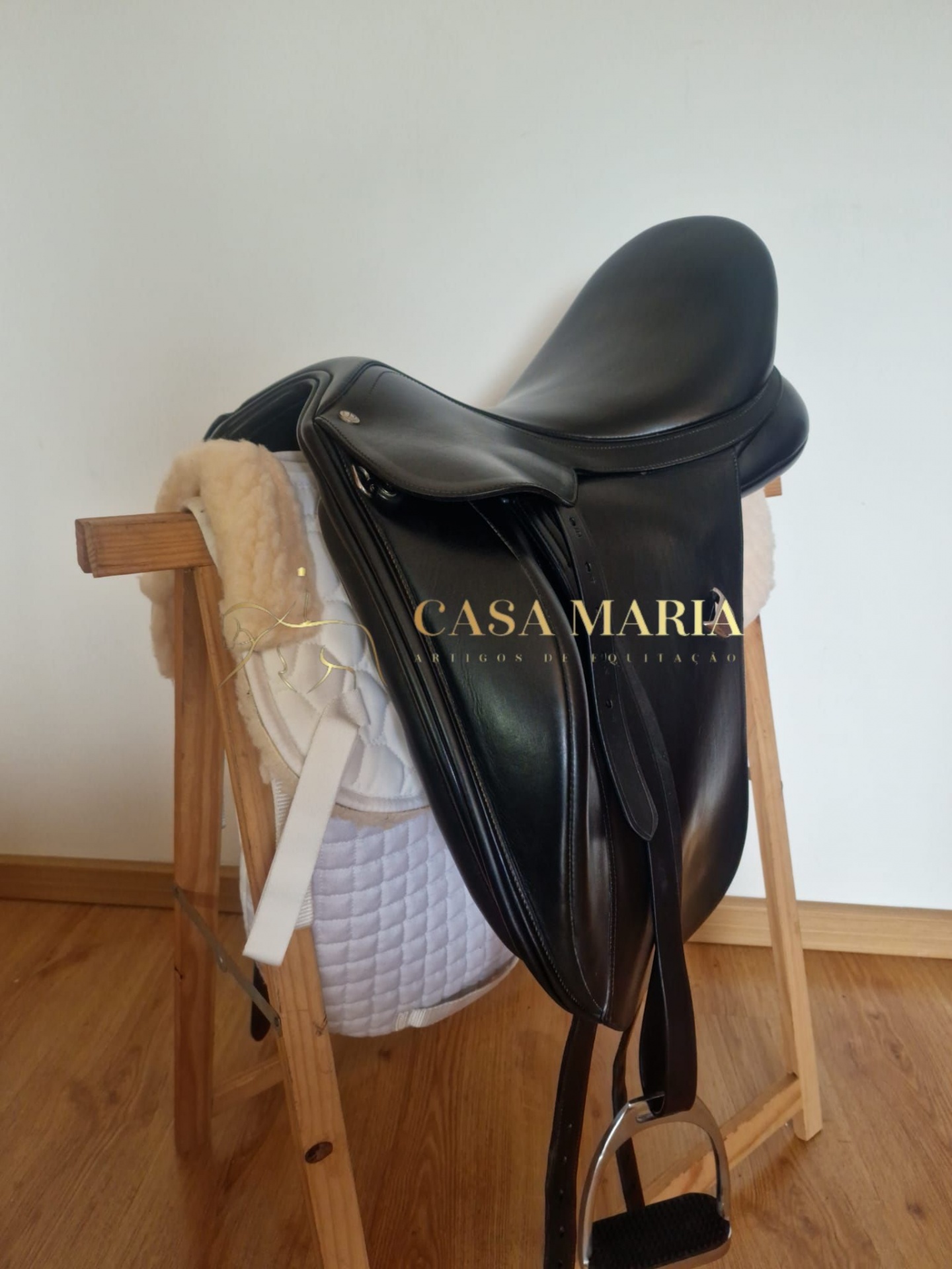 Sela de equitação preta em couro com manta branca num suporte de madeira