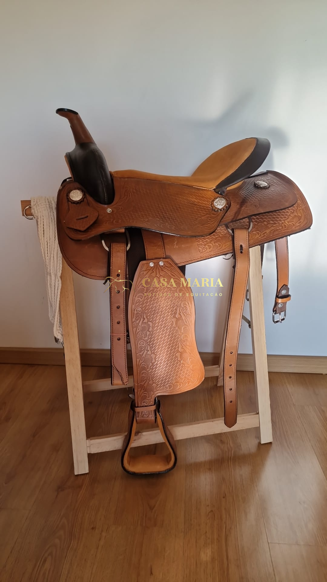 Sela de montaria em couro castanho claro detalhado num suporte de madeira