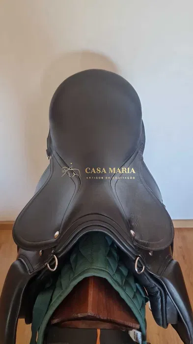 Sela de equitação preta em couro com almofada verde sobre suporte de madeira