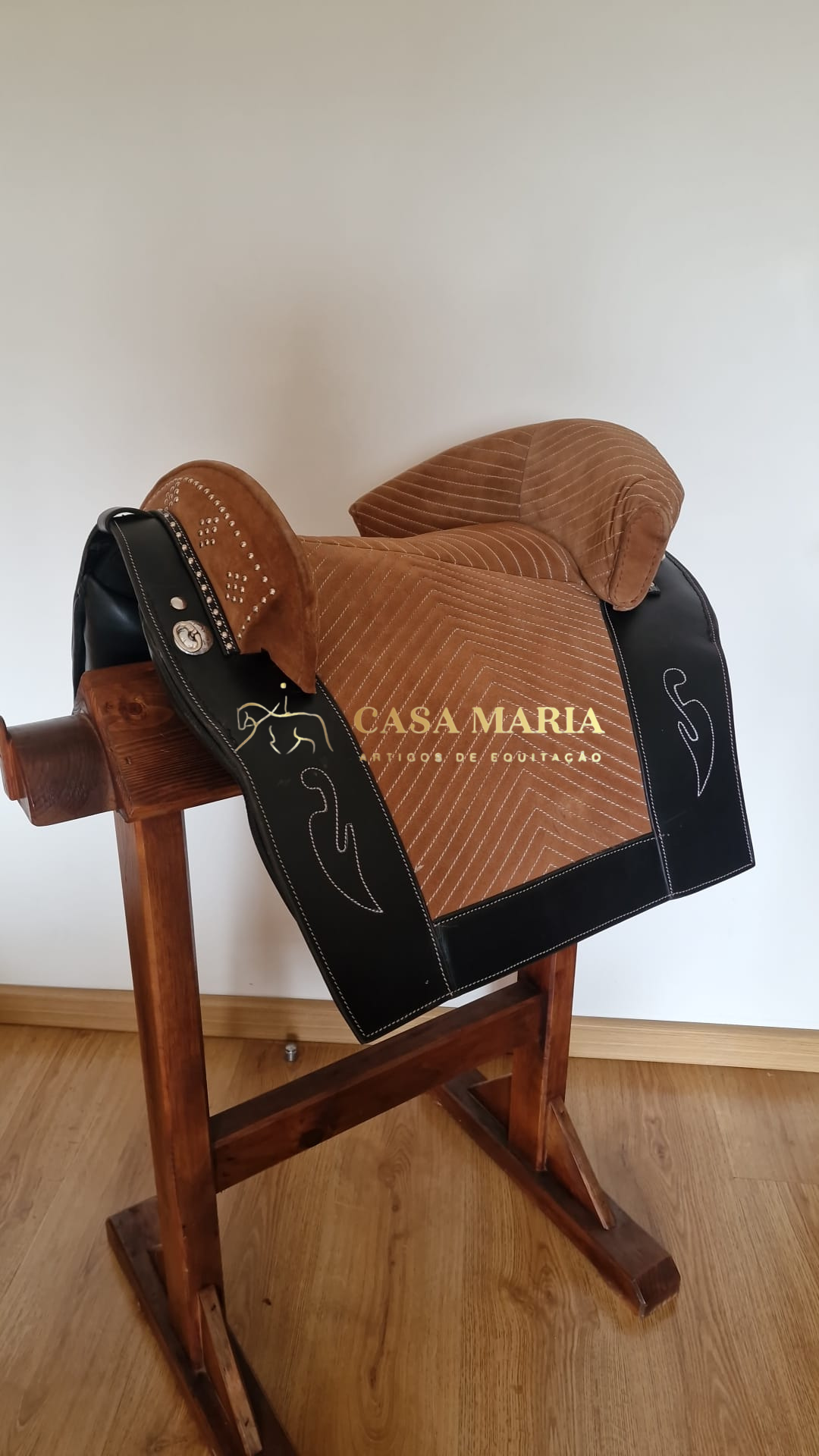 Sela equestre castanha e preta com padrões acolchoados e bordados branco num suporte de madeira