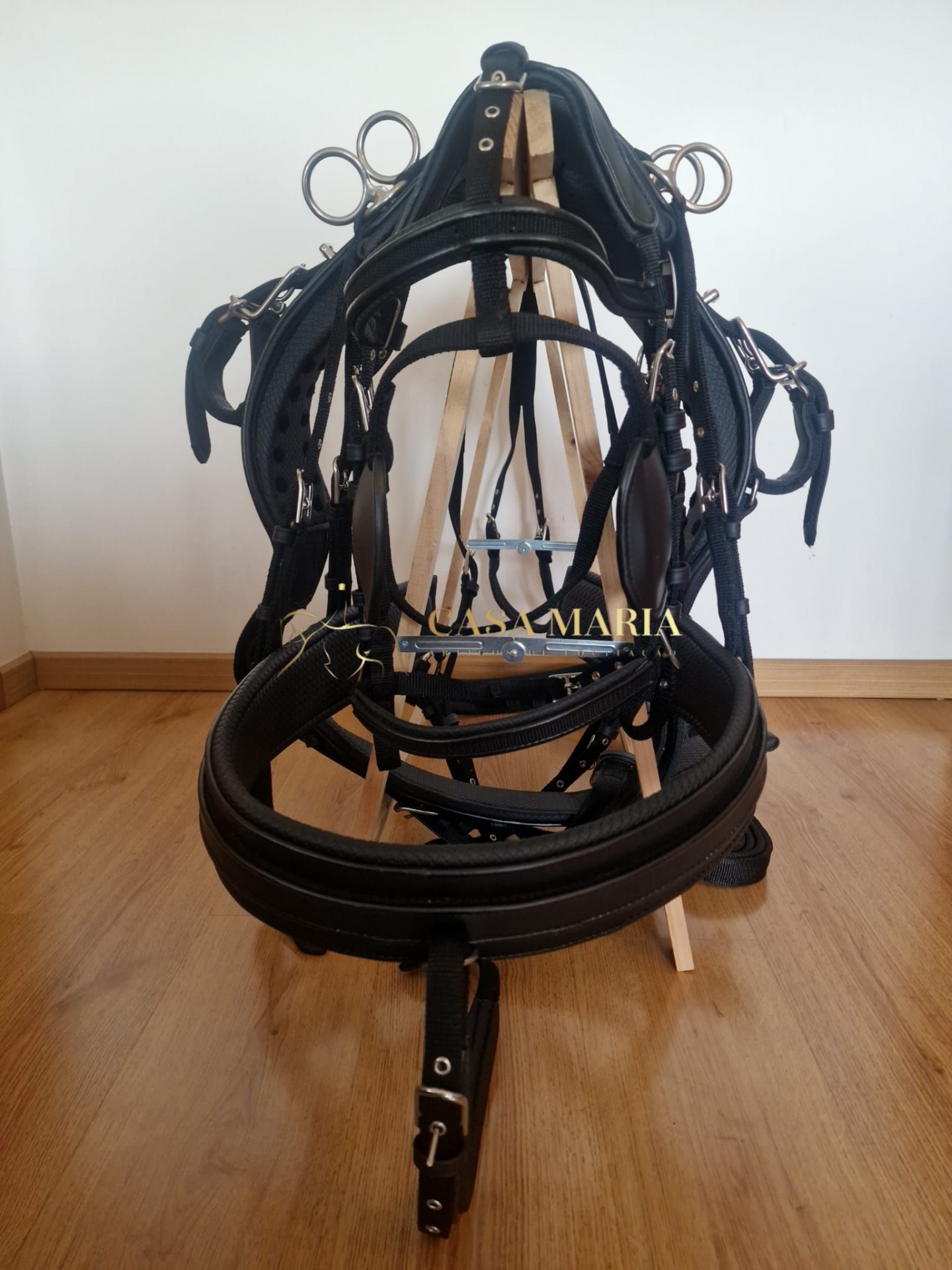 Cabeçada equina preta em couro com fivelas e ilhós metálicos pendurada em suporte