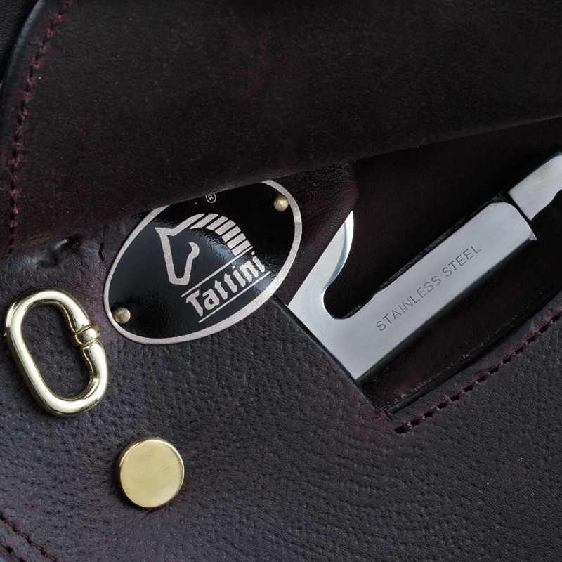 Detalhe de artigo em pele preta com textura granulada, metais dourado e prateado, chapa oval 'Tatini' e texto 'STAINLESS STEEL'.