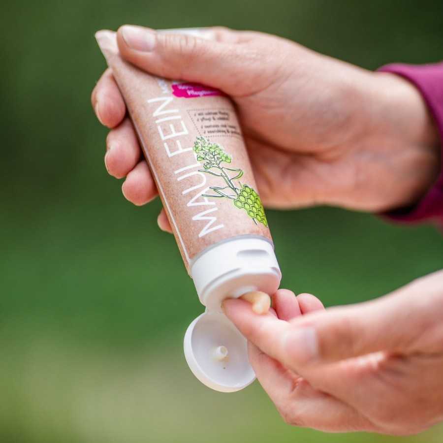 Tubo de creme rosa com tampa branca e texto MAUI FEIN sendo espreme por uma mão.