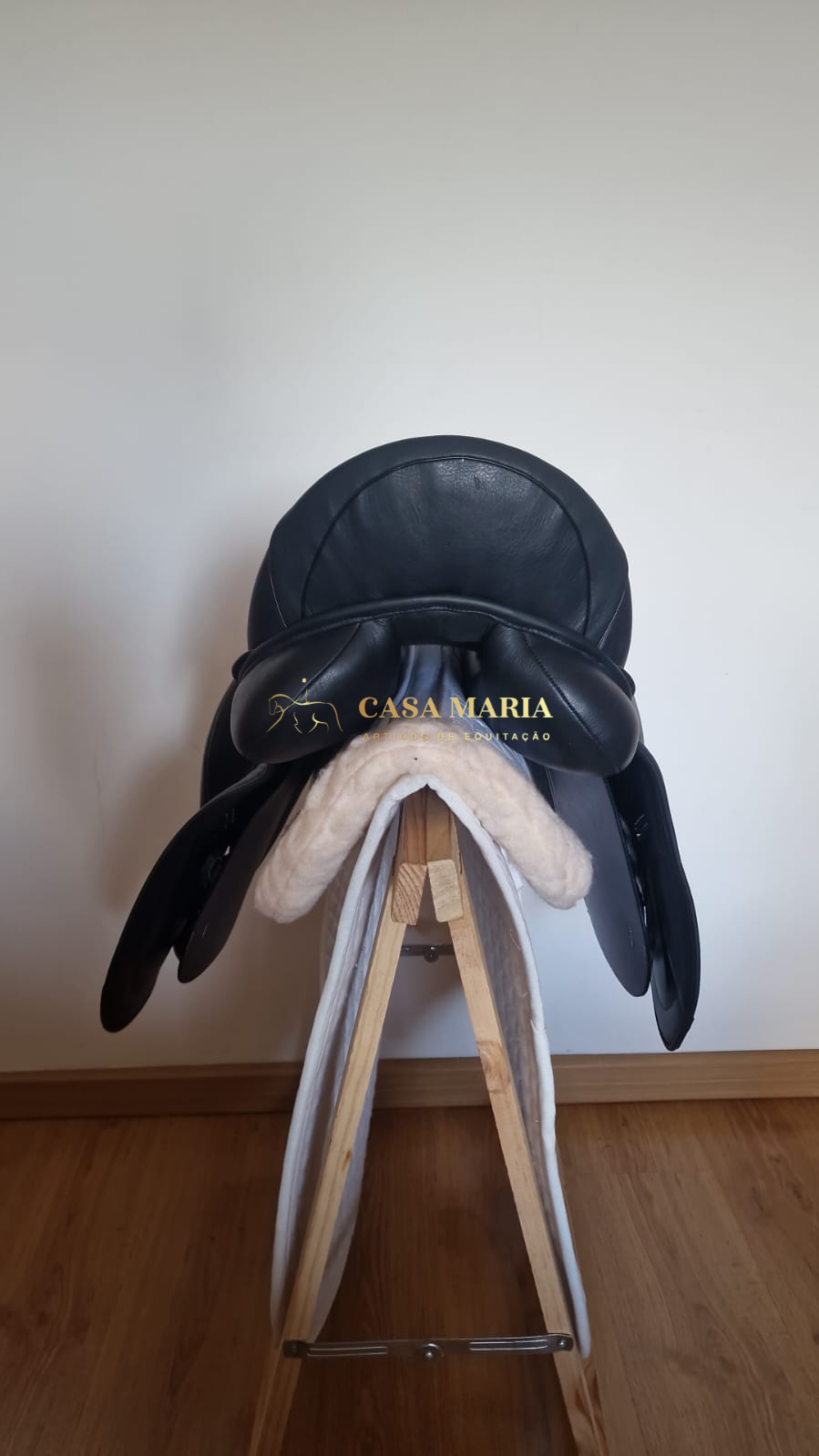 Sela de equitação preta em couro sobre almofada branca e suporte de madeira