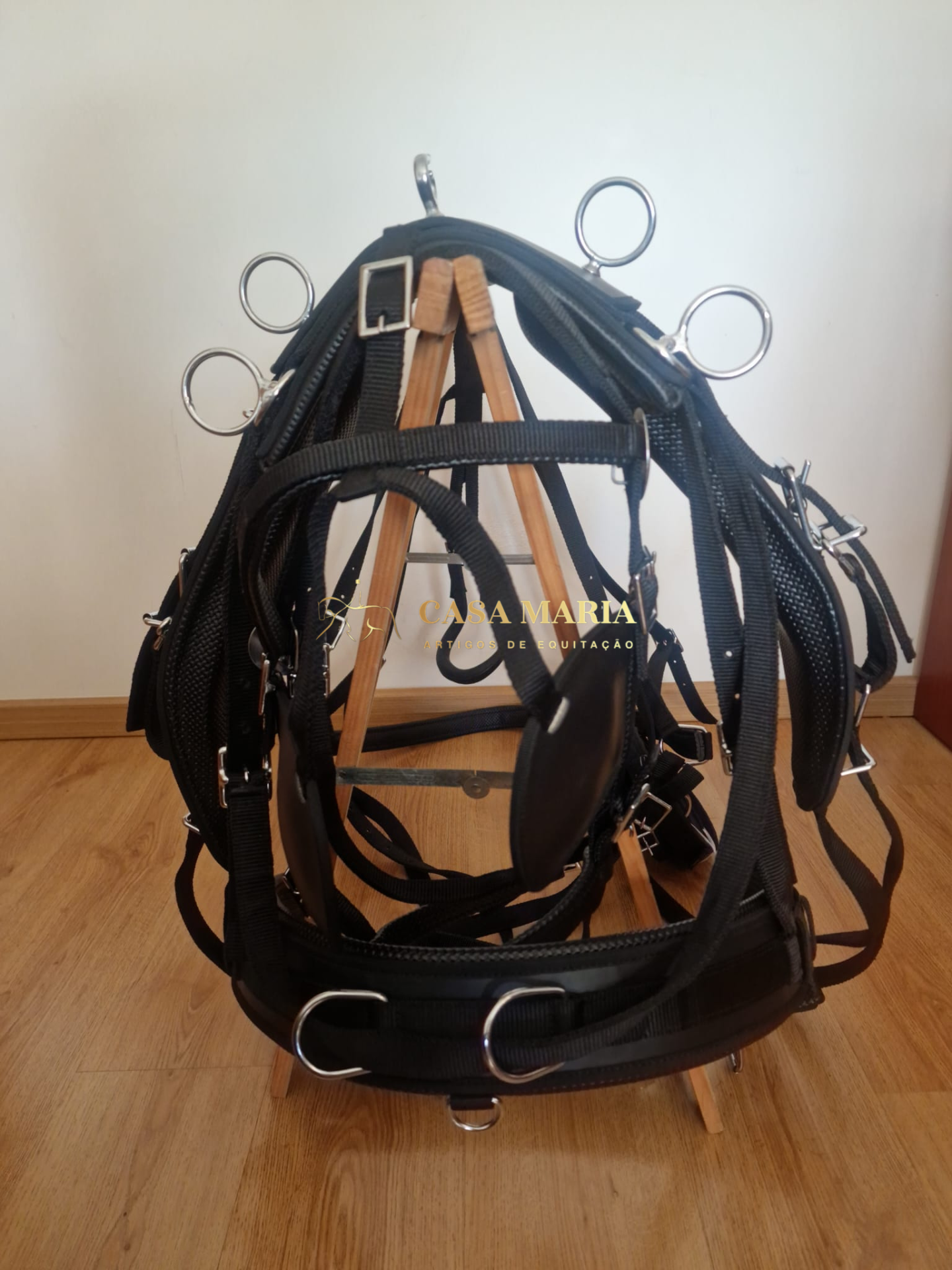 Arreio equestre preto com fivelas metálicas pendurado num cavalete de madeira