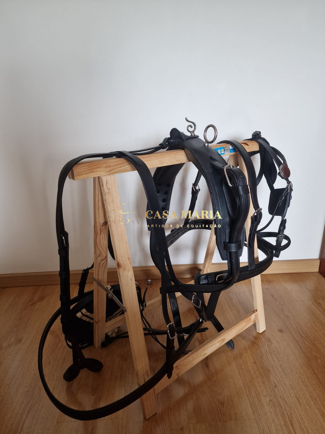 Arreio de couro preto pendurado em suporte de madeira