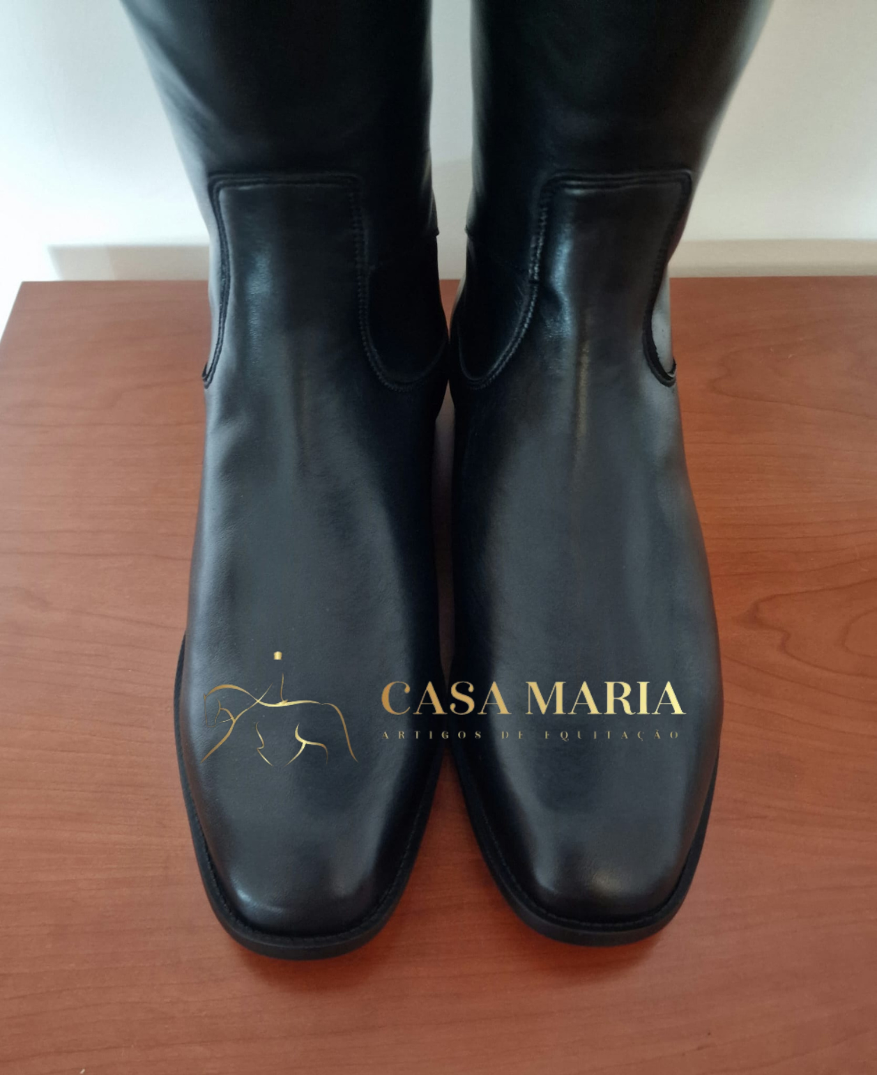 Botas pretas de couro com biqueira quadrada sobre madeira clara, logotipo CASA MARIA na imagem