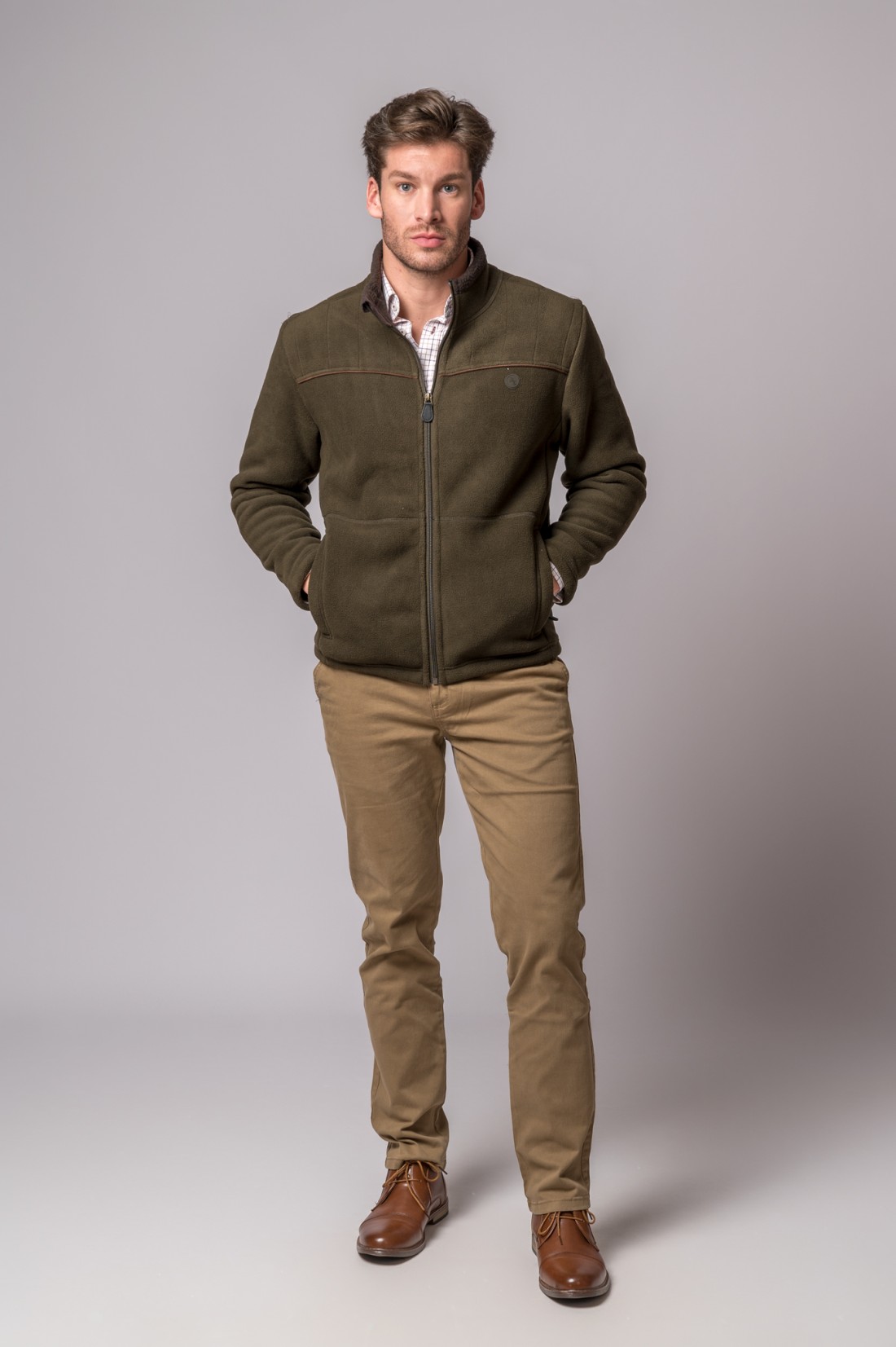 Homem com casaco polar verde-oliva e calças khaki em fundo cinzento