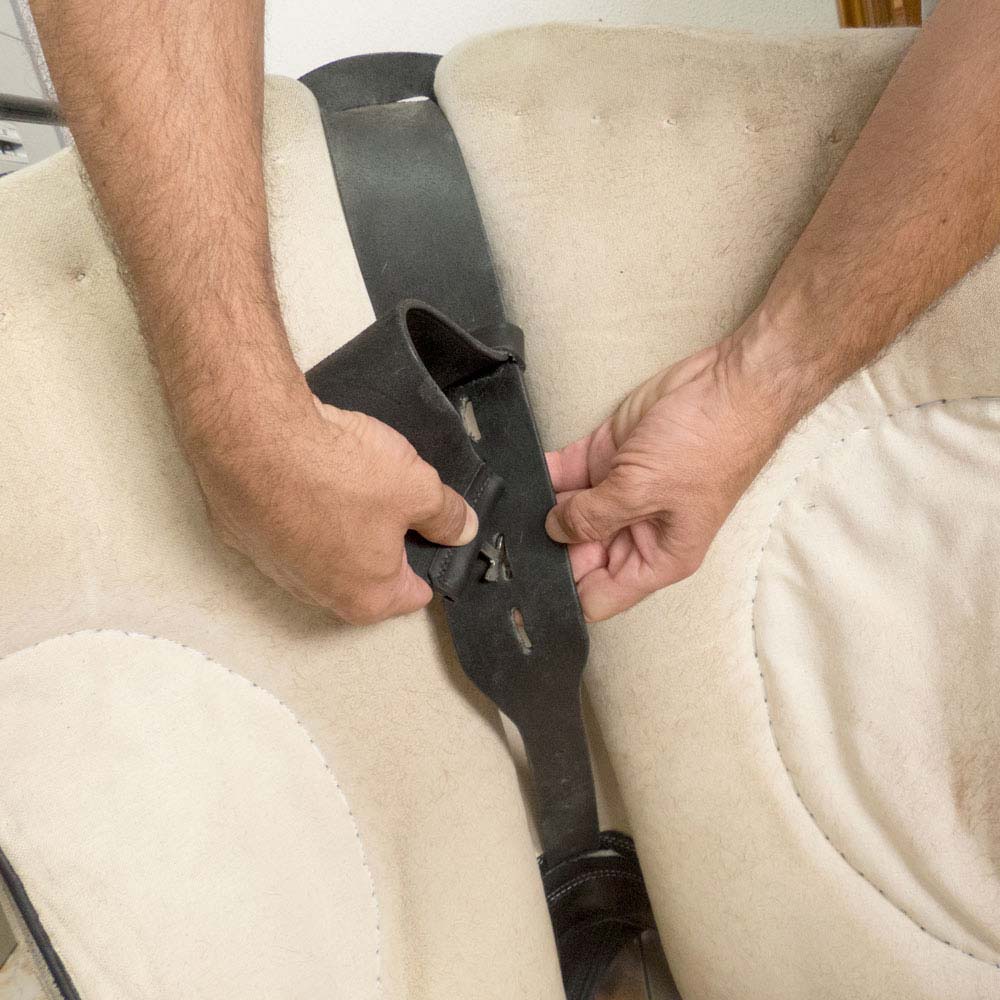 Correia de couro preta a ser ajustada numa cadeira bege por duas mãos