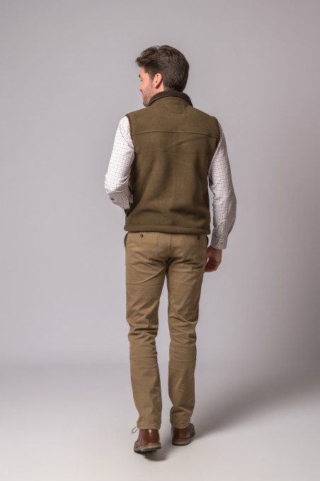 Homem de costas com colete castanho, camisa branca quadriculada, calças castanhas e sapatos castanhos