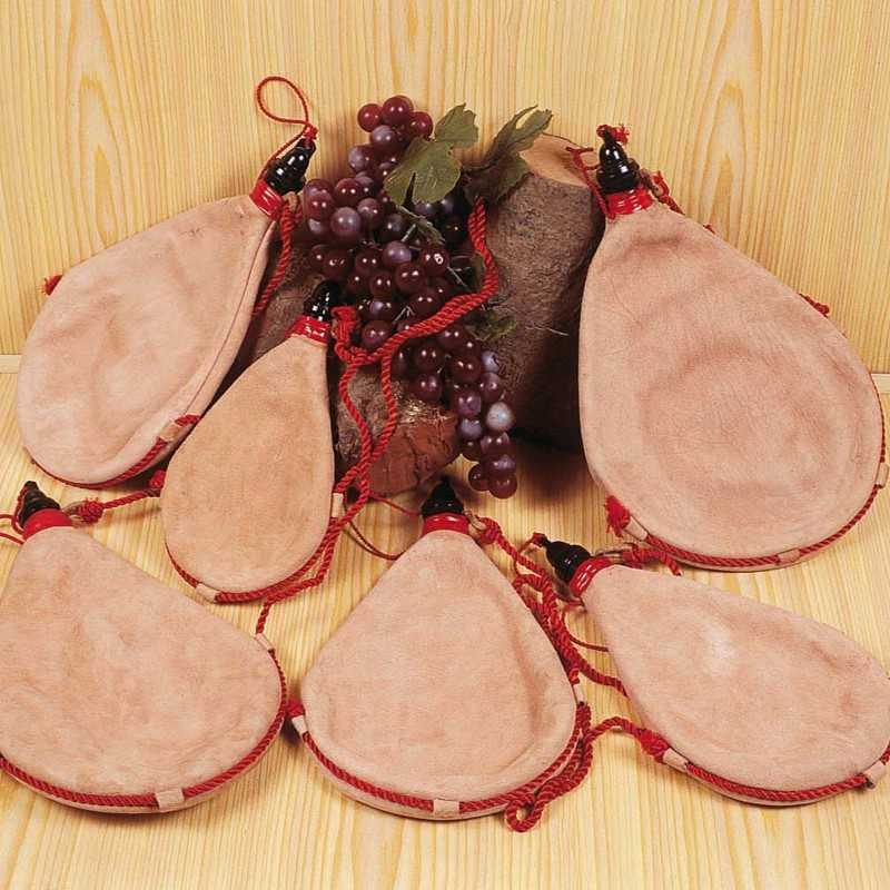 Sete odres de couro cor de pele com detalhes vermelhos e ramo decorativo de uvas roxas sobre madeira