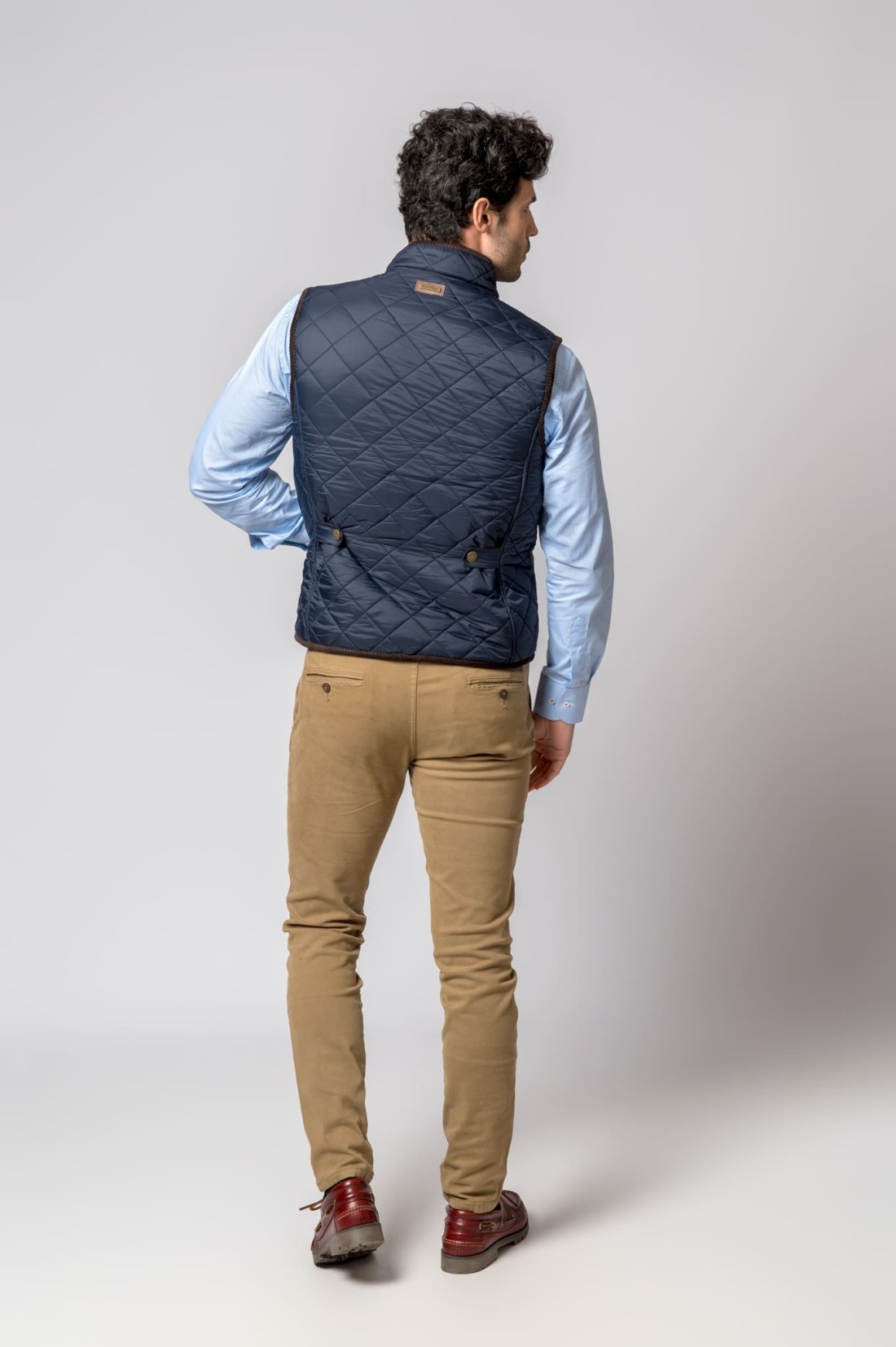 Homem de casaco azul escuro, camisa azul clara, calças bege e sapatos castanhos visto de costas