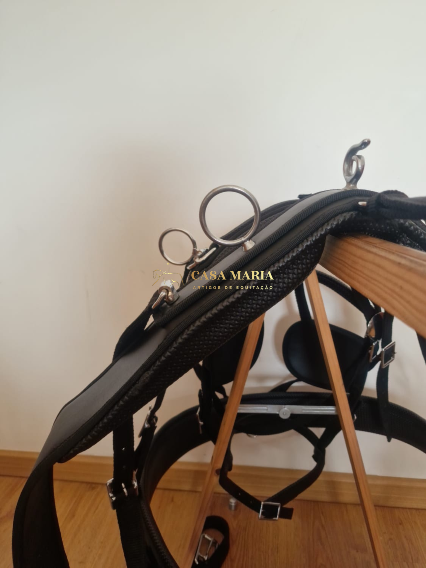 Sela de equitação preta com argolas metálicas sobre suporte de madeira