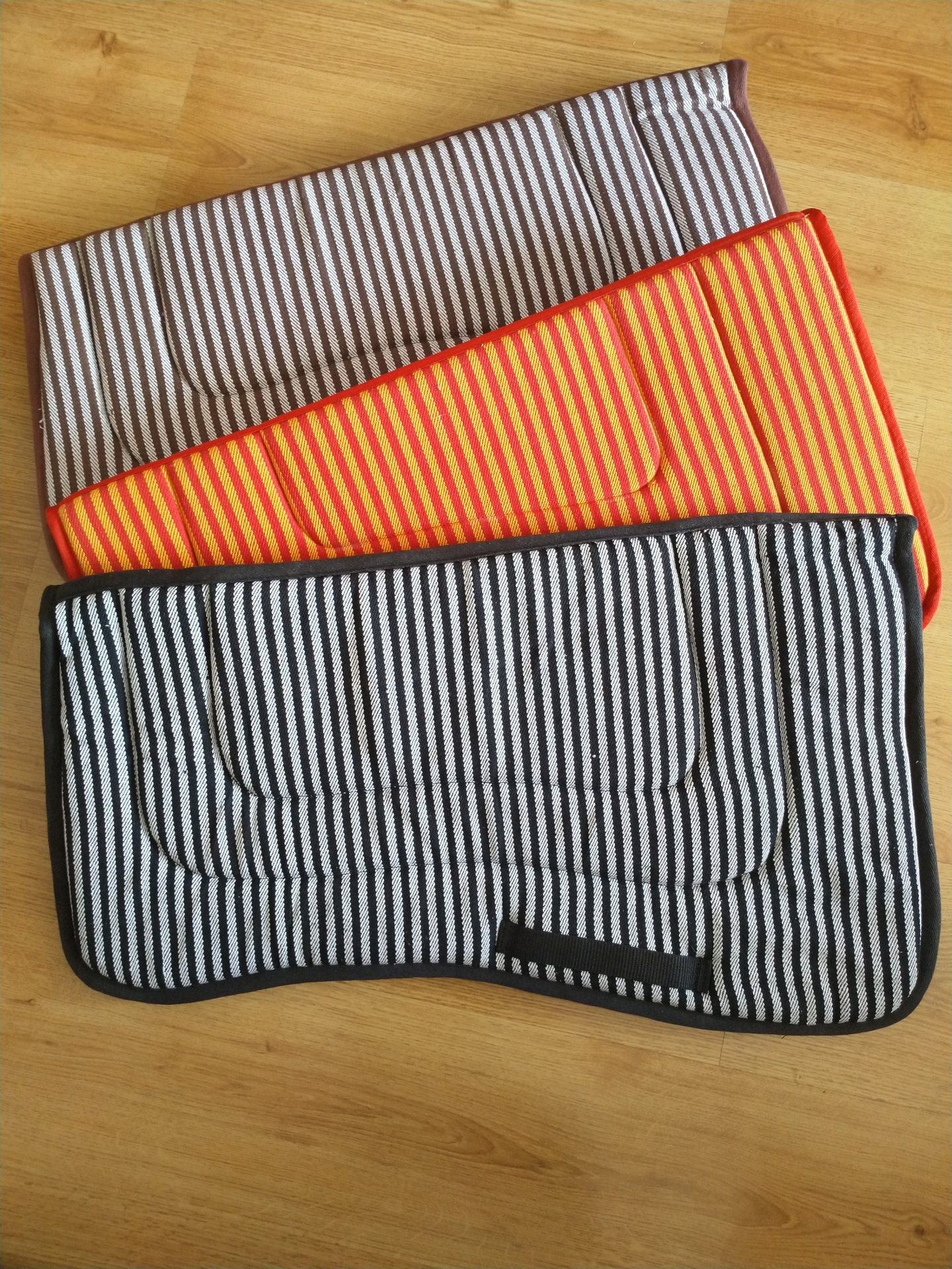 Três mantas de cavalo listradas em diferentes cores sobre pavimento de madeira clara