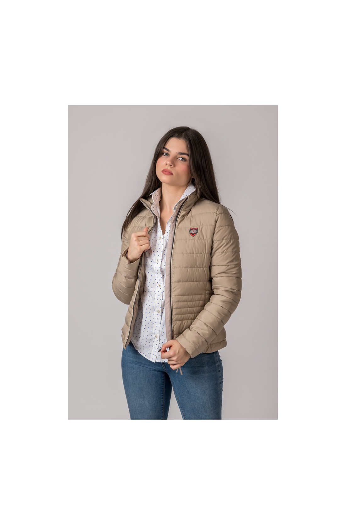 Mulher com casaco bege acolchoado, camisa branca de pontos azuis e jeans azuis