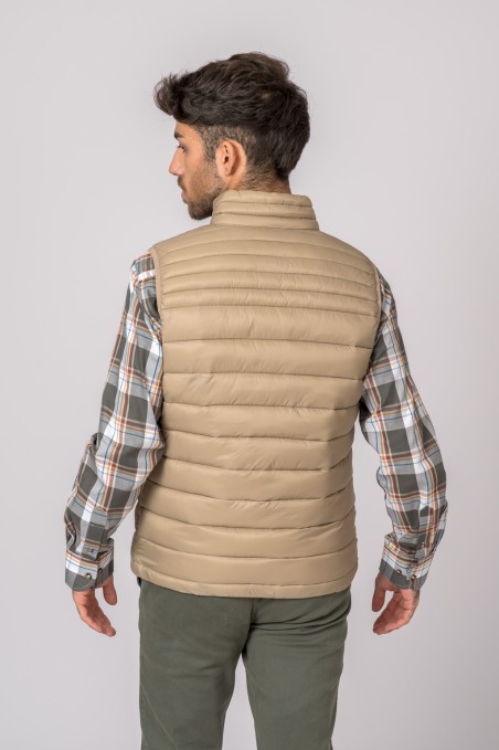 Homem de costas usando colete acolchoado bege e camisa xadrez com calças verdes