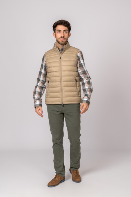 Homem com colete bege acolchoado, camisa xadrez, calças castanho-oliva e sapatos castanhos