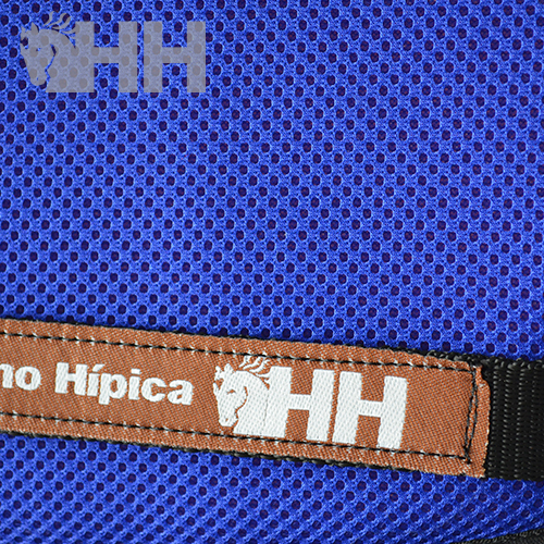 Etiqueta de tecido castanha com texto Hípica HH numa superfície de tecido azul tipo rede