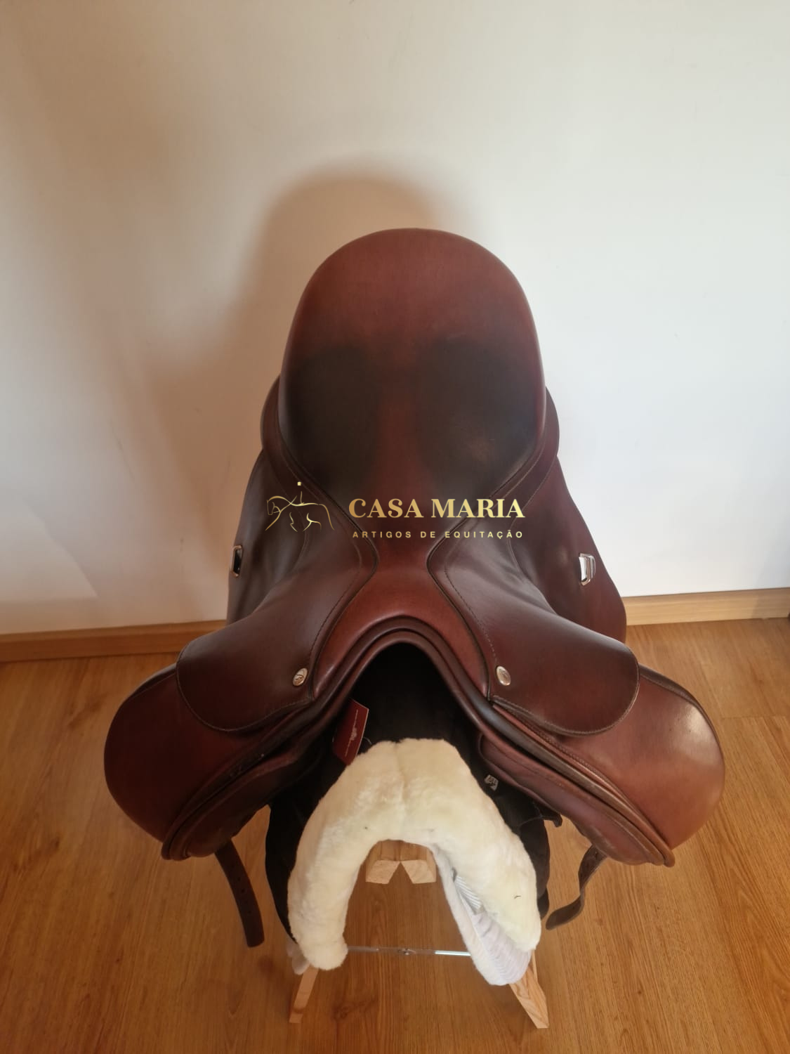 Sela castanha de equitação em couro sobre suporte de madeira com forro branco