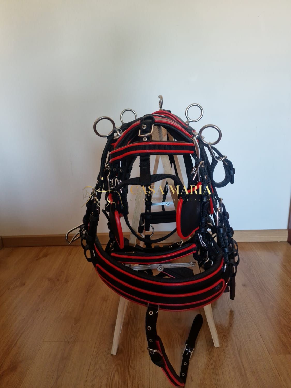 Sela para cavalo preta com detalhes vermelhos pendurada numa cadeira