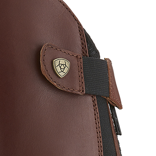 close-up de bota castanha com emblema metálico e fecho de velcro e tira elástica preta