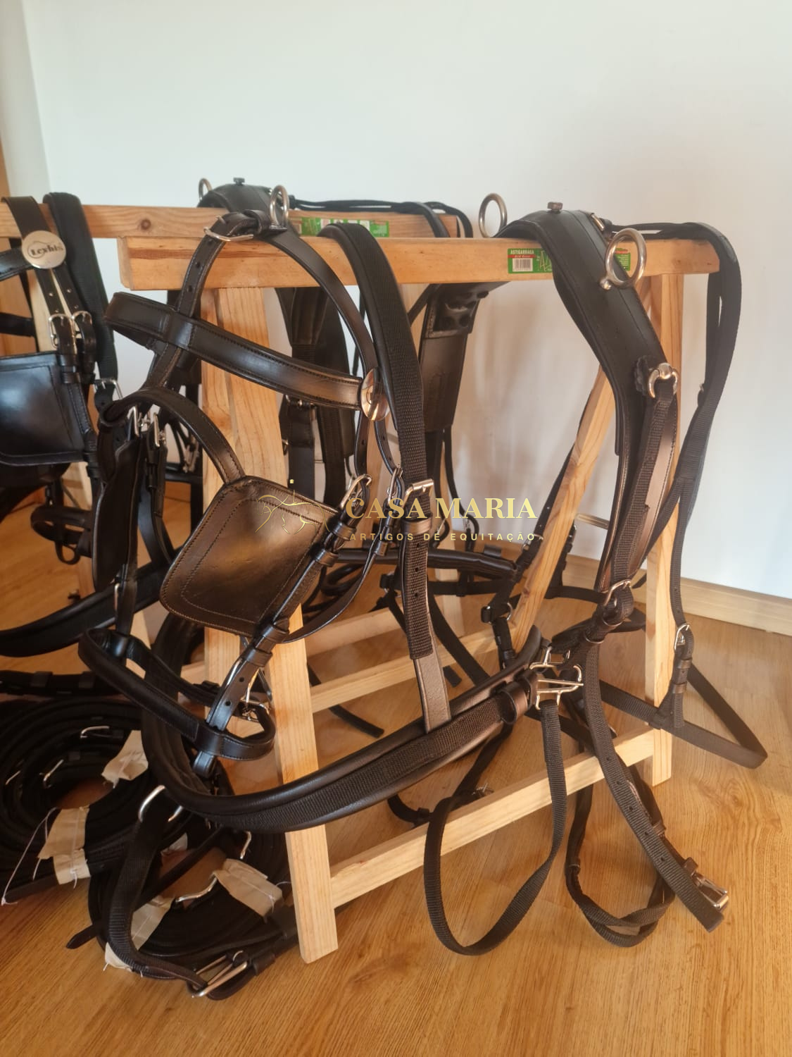 Arreios pretos de couro pendurados em suporte de madeira