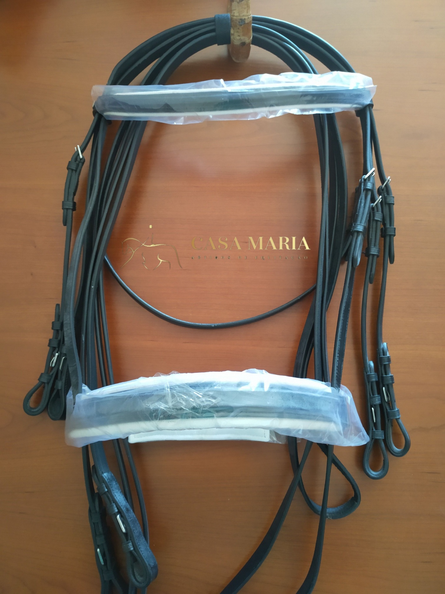 Cabeçada de couro preta com acolchoamento em plástico sobre superfície de madeira