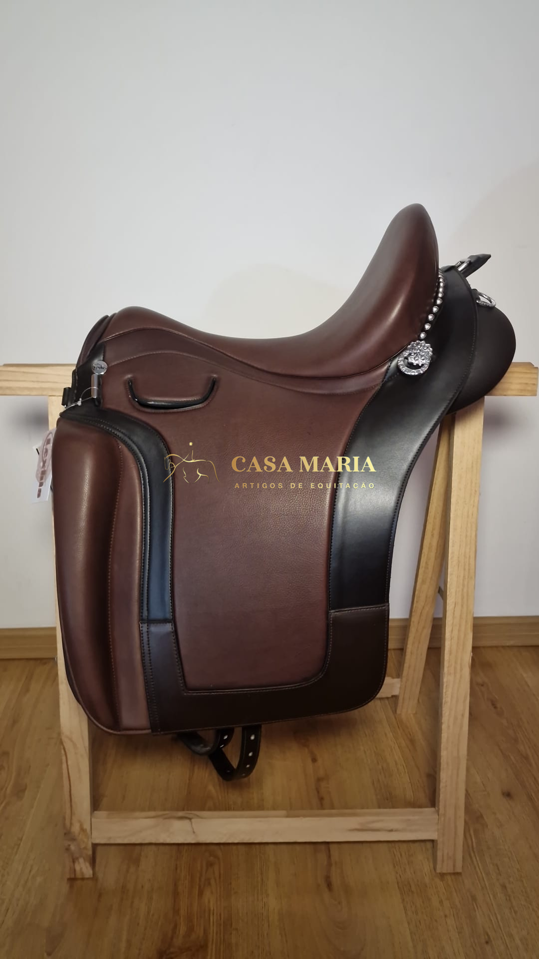 Selim de equitação castanho e preto com detalhes metálicos, sobre estrutura de madeira