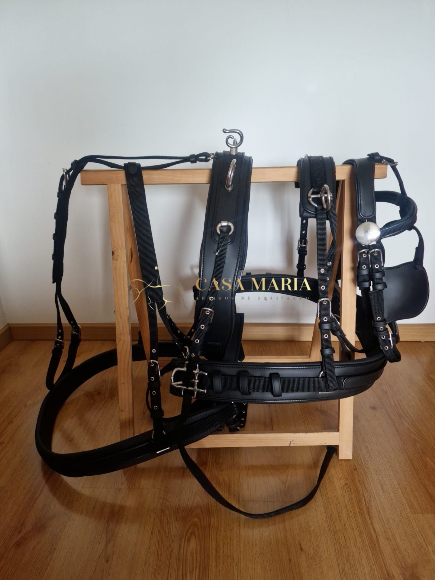 Arnês preto para equitação com fivelas metálicas pendurado numa estrutura de madeira