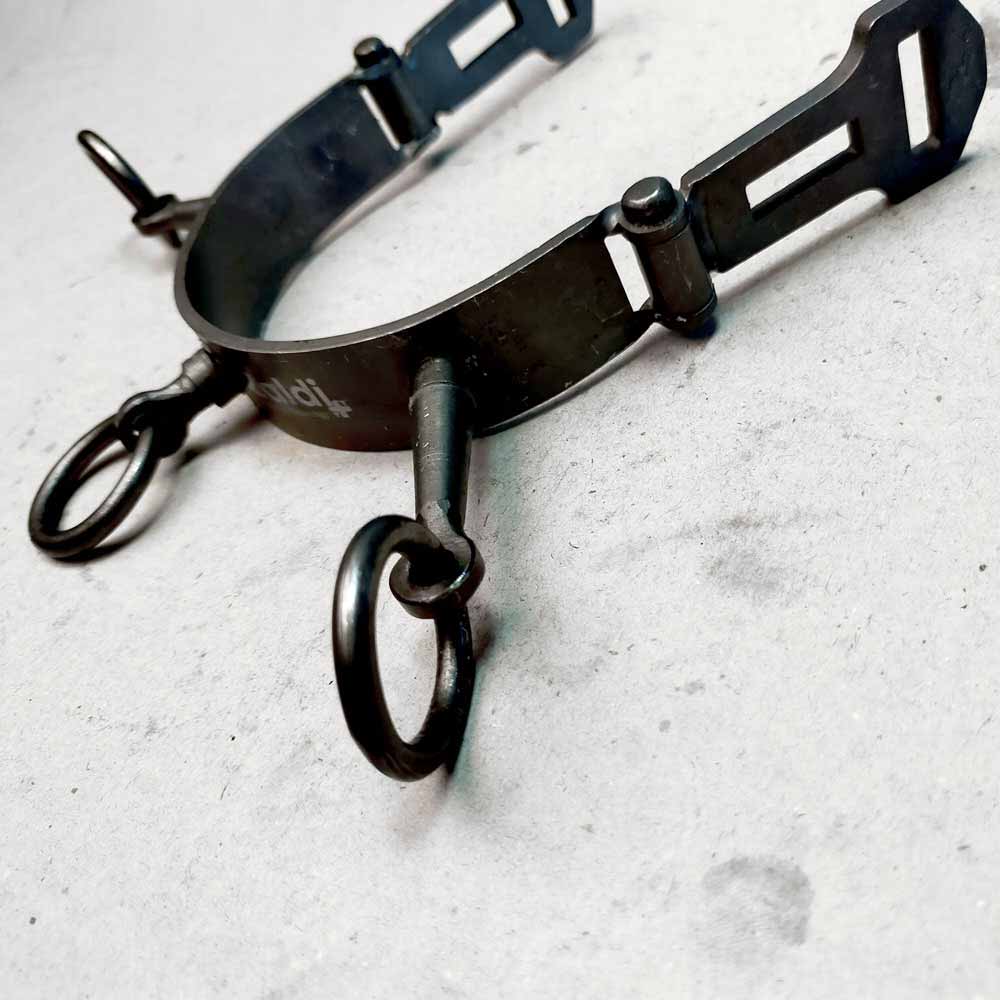 Espora metálica preta com argolas sobre piso cinza