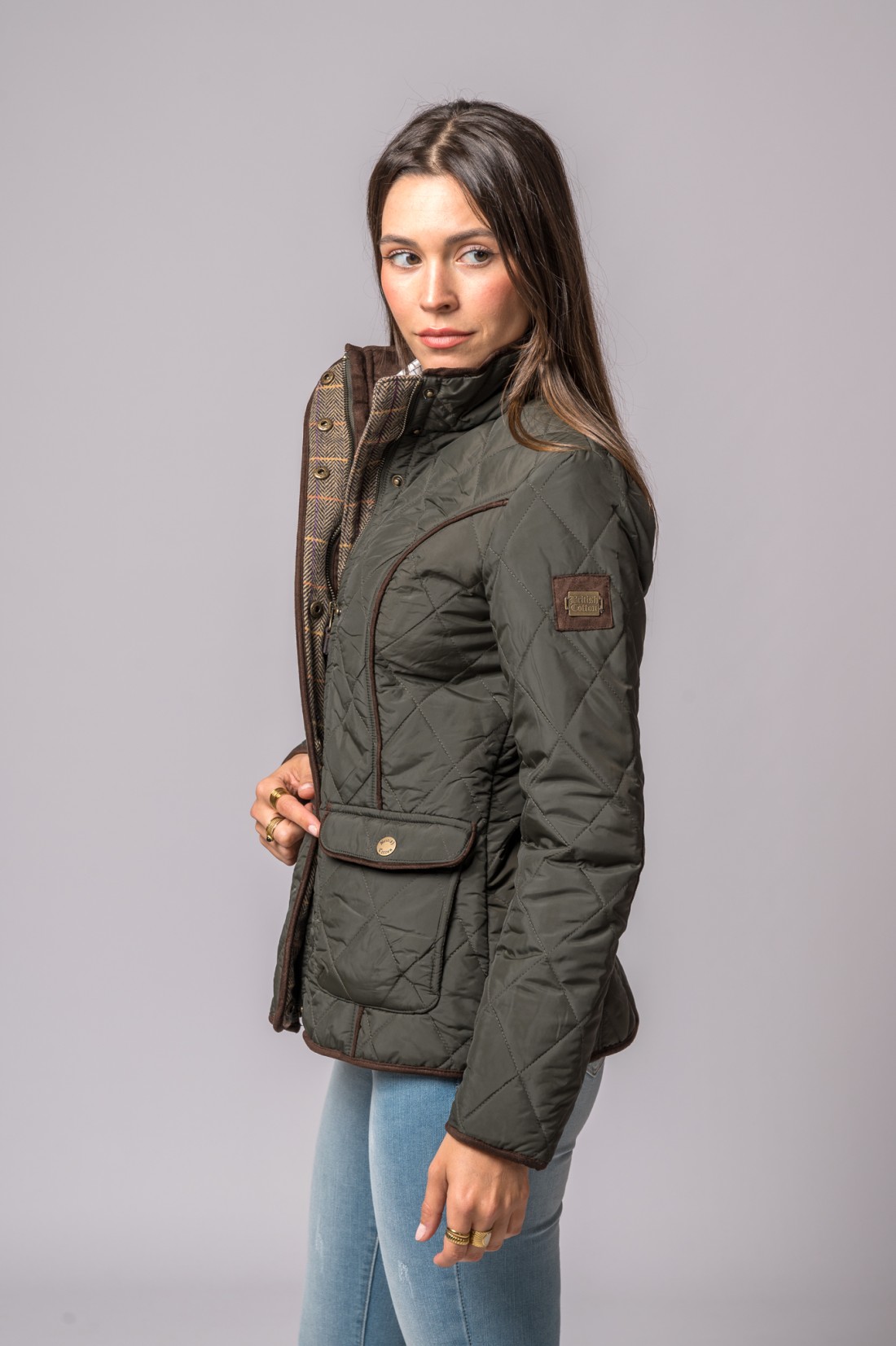 Casaco feminino verde-escuro matelassé com interior xadrez, detalhes castanhos e etiqueta British Cotton no braço.