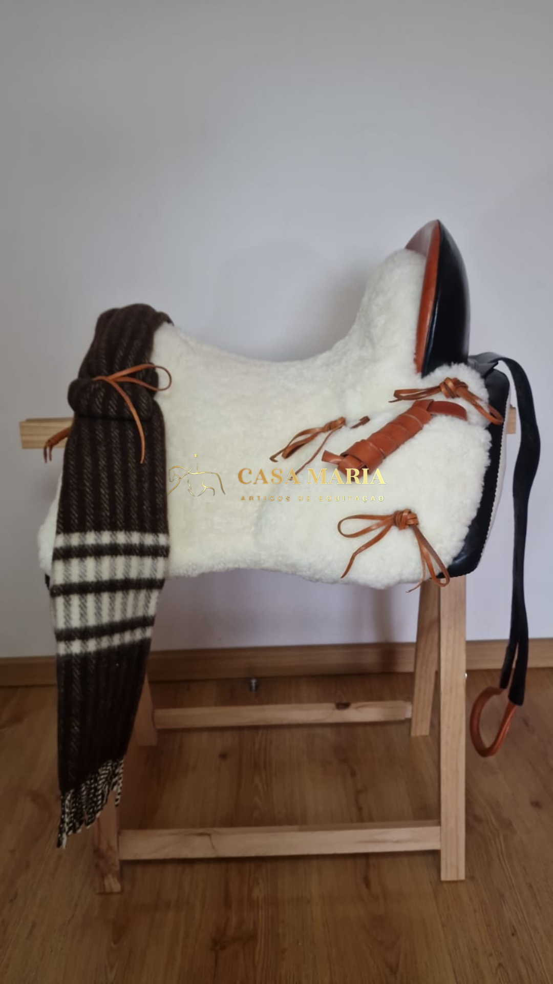 Sela de equitação branca com detalhes em couro castanho e preto sobre suporte de madeira
