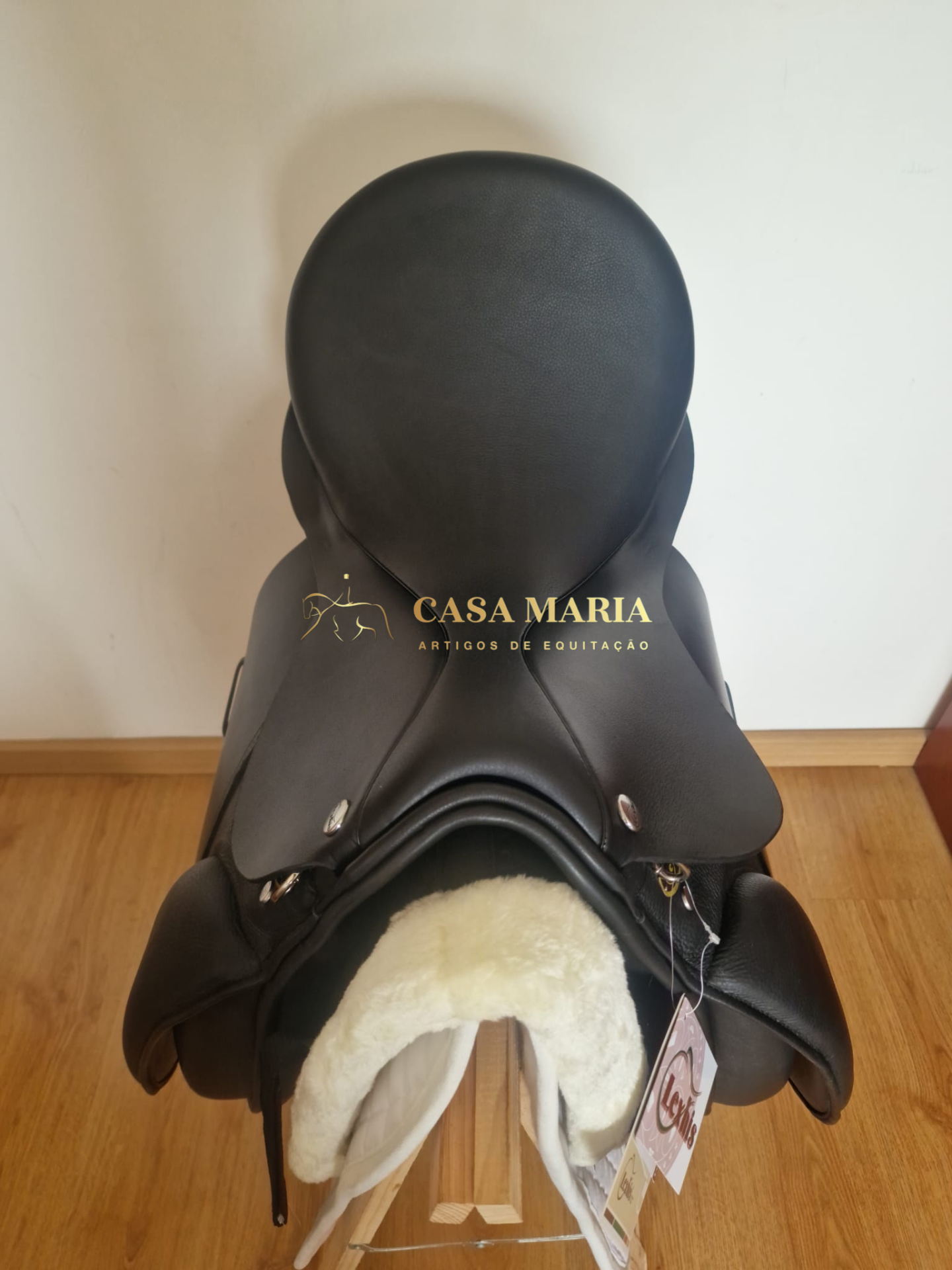 Sela de equitação preta em couro com revestimento felpudo branco em suporte de madeira