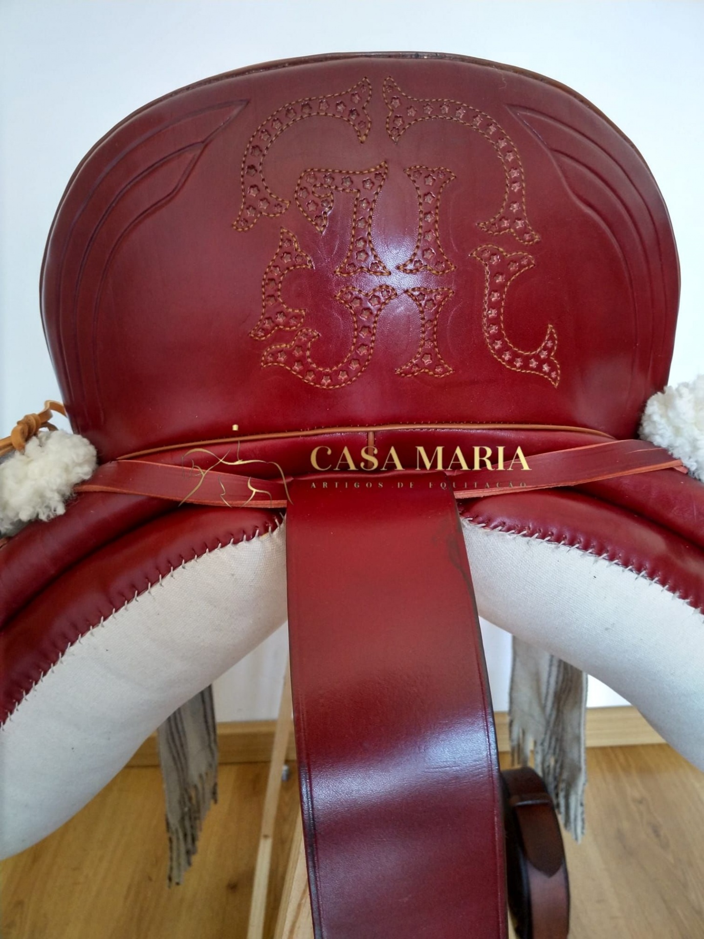 Sela de montaria vermelha com detalhes em branco sobre suporte de madeira