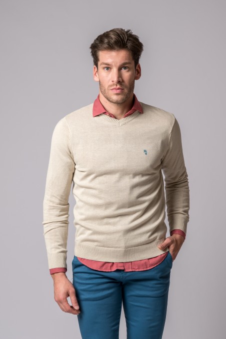 Homem com camisola bege e camisa vermelha com calças azul-turquesa sobre fundo cinza