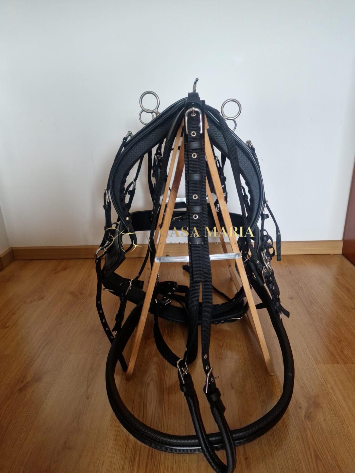 Bridão de cavalo preto com partes metálicas sobre estrutura de madeira